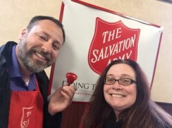 Man in woman in front of Salvation Army sign with bell